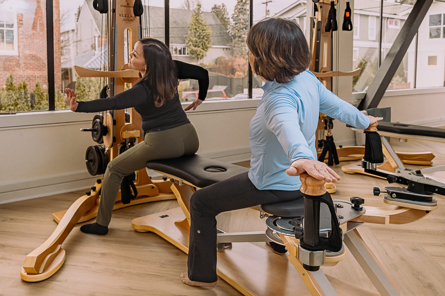 Two women exercising on Pilates reformers in a bright studio.