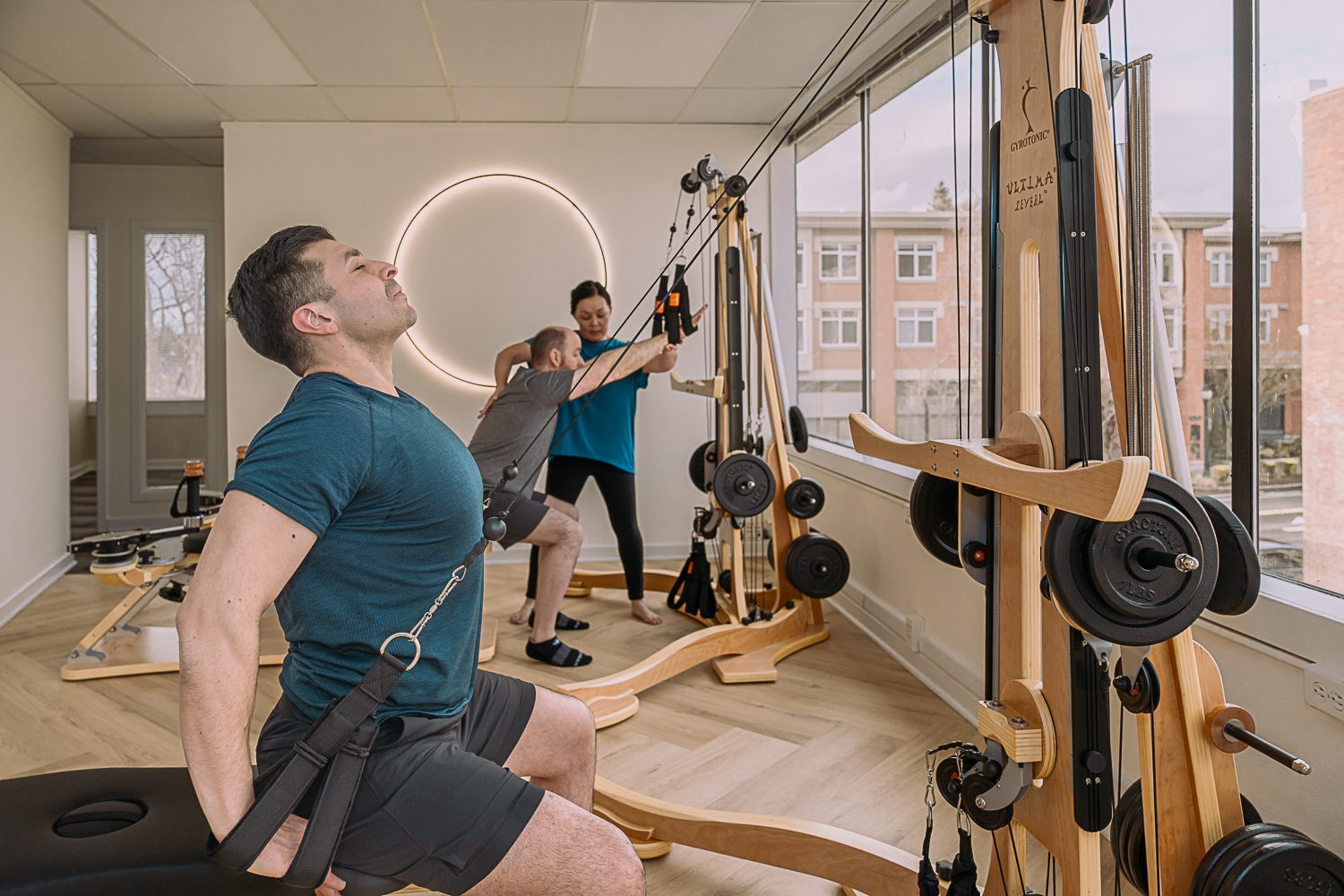 Three men exercising with resistance bands on wooden wall-mounted equipment.