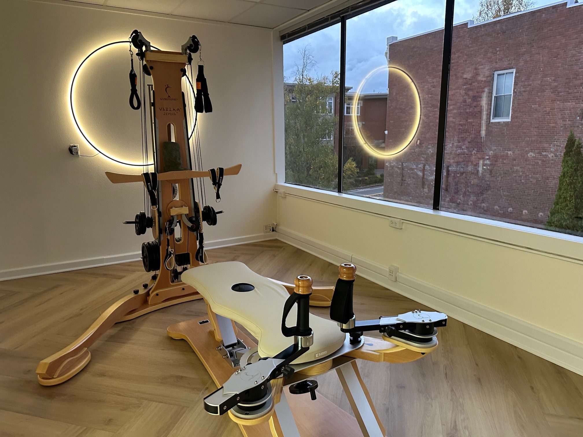 A sleek rowing machine with a wooden frame and illuminated circular wall lights.