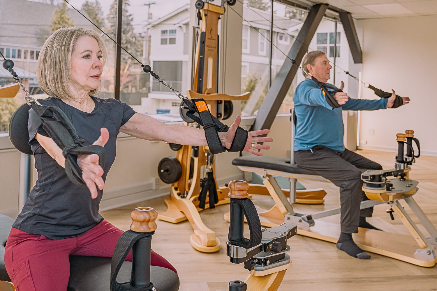 Two people exercising with resistance bands in a bright gym.